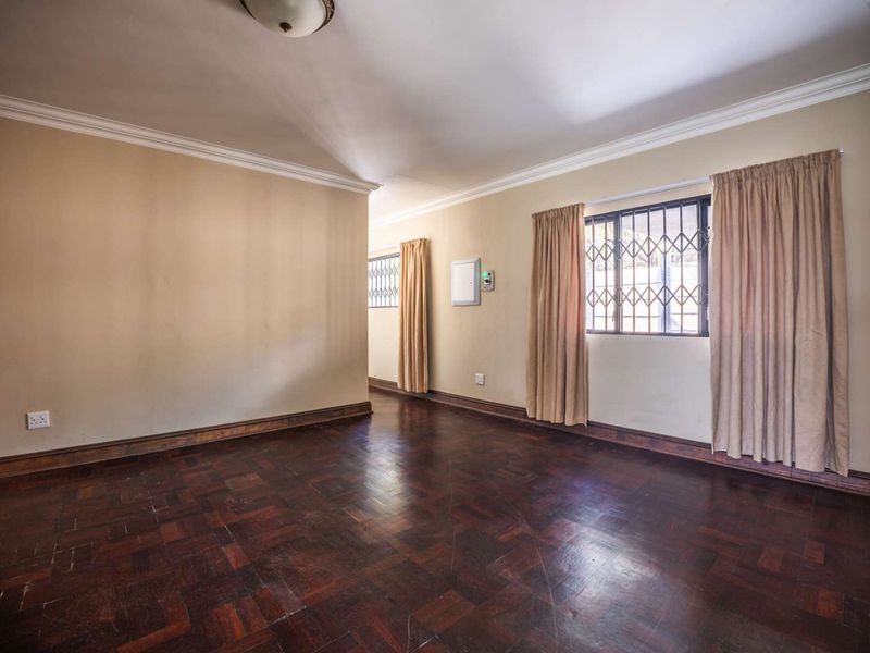An empty living room featuring dark parquet flooring, crown molding, and security bars on the windows.