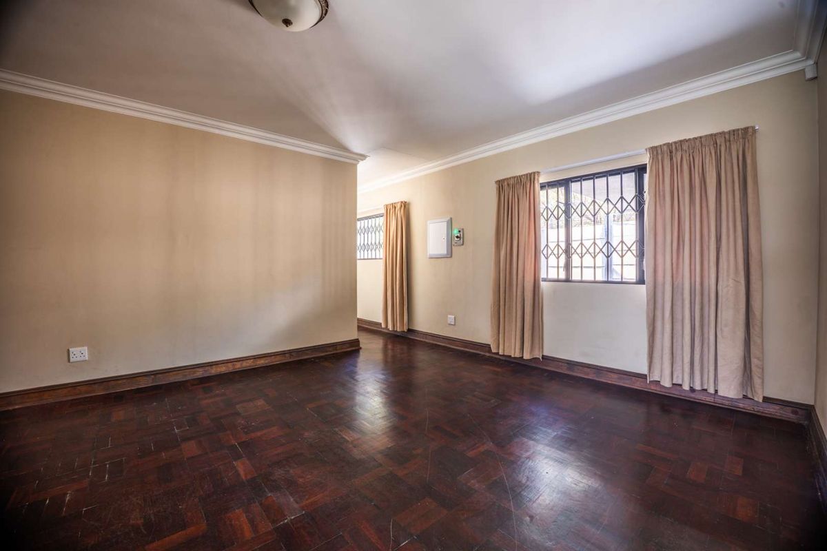 An empty living room featuring dark parquet flooring, crown molding, and security bars on the windows.