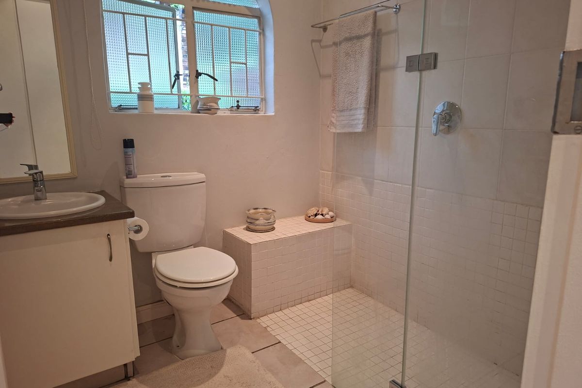 A functional bathroom featuring a walk-in shower with glass screen, vanity cabinet with basin, and a toilet, finished with tiled walls and flooring.