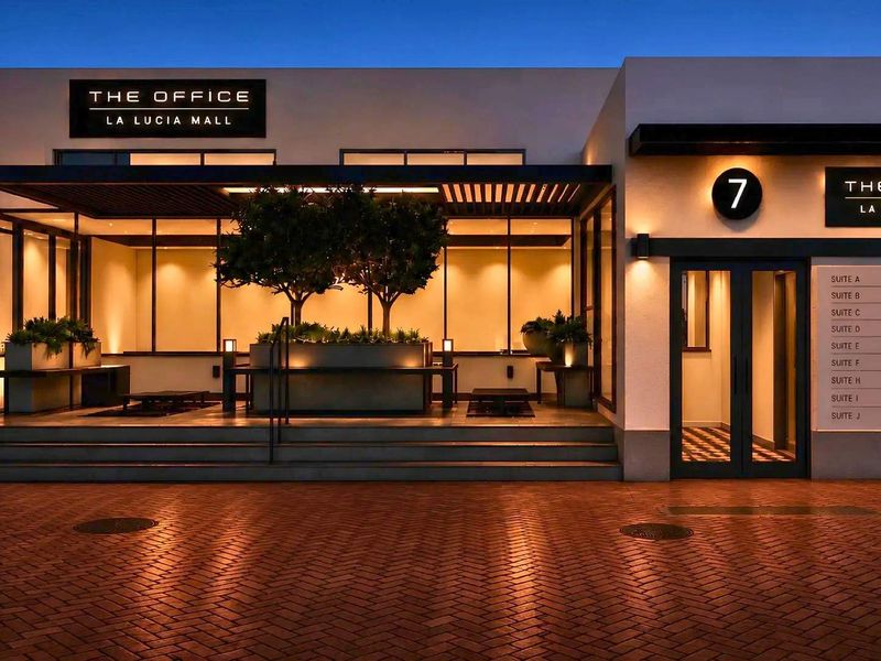 Modern office building entrance at La Lucia Mall featuring a paved driveway, covered patio area, and professional exterior signage.