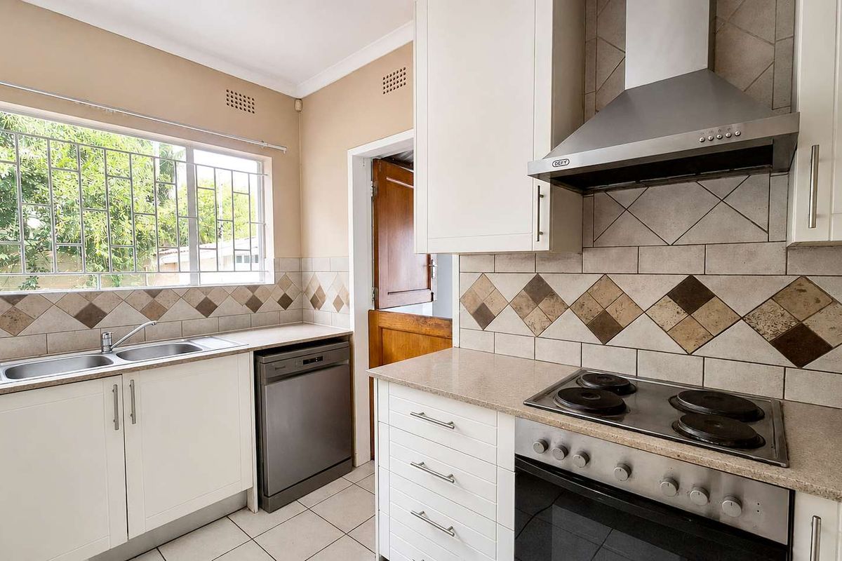 Functional kitchen featuring white cabinetry, stone-look countertops, stainless steel oven with extractor fan, and a double basin sink with security-barred window.