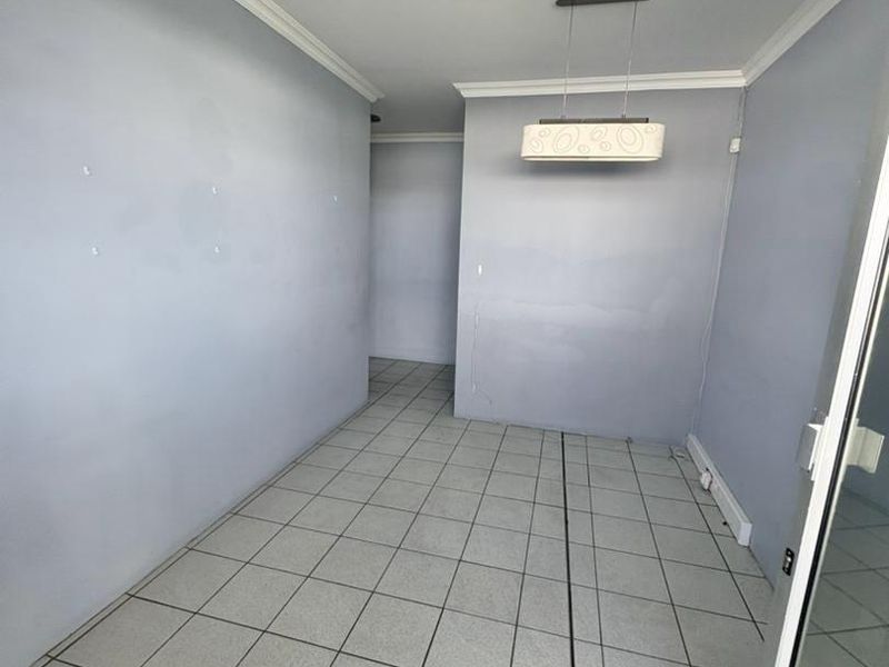 An empty office space featuring tiled flooring, neutral wall paint, and a modern pendant light fixture, suitable for a professional workspace.