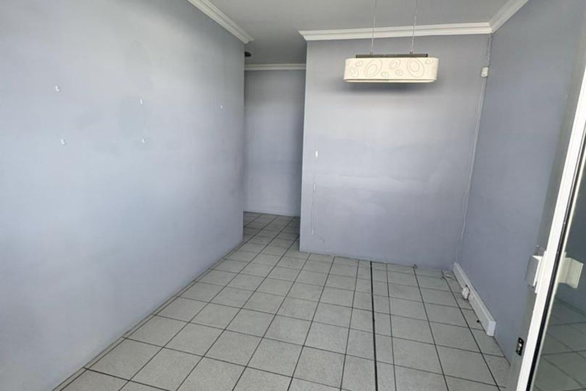 An empty office space featuring tiled flooring, neutral wall paint, and a modern pendant light fixture, suitable for a professional workspace.