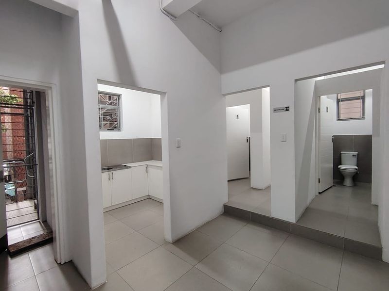 Office interior featuring a kitchenette area, tiled flooring, and private restroom facilities with modern white finishes.