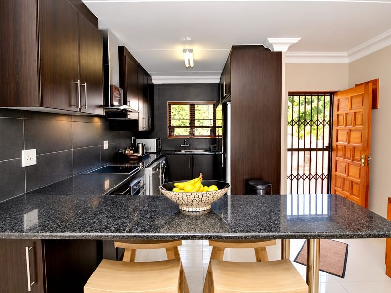 Modern kitchen featuring dark wood cabinetry, granite countertops, integrated appliances, and a breakfast bar, with direct access to the exterior.