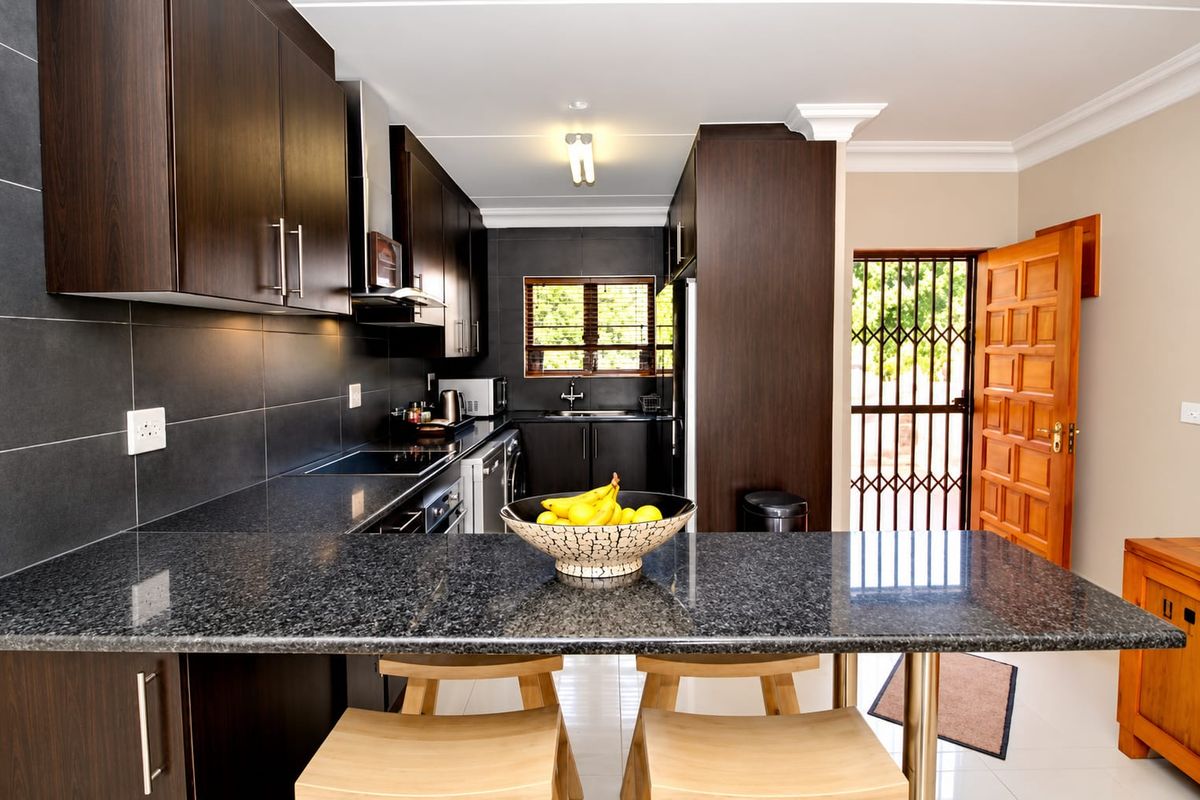 Modern kitchen featuring dark wood cabinetry, granite countertops, integrated appliances, and a breakfast bar, with direct access to the exterior.