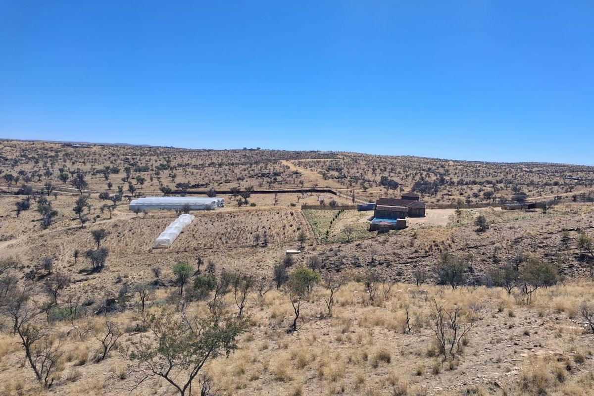 Aerial view of the small holding property featuring multiple greenhouses, outbuildings, and expansive arid landscape.
