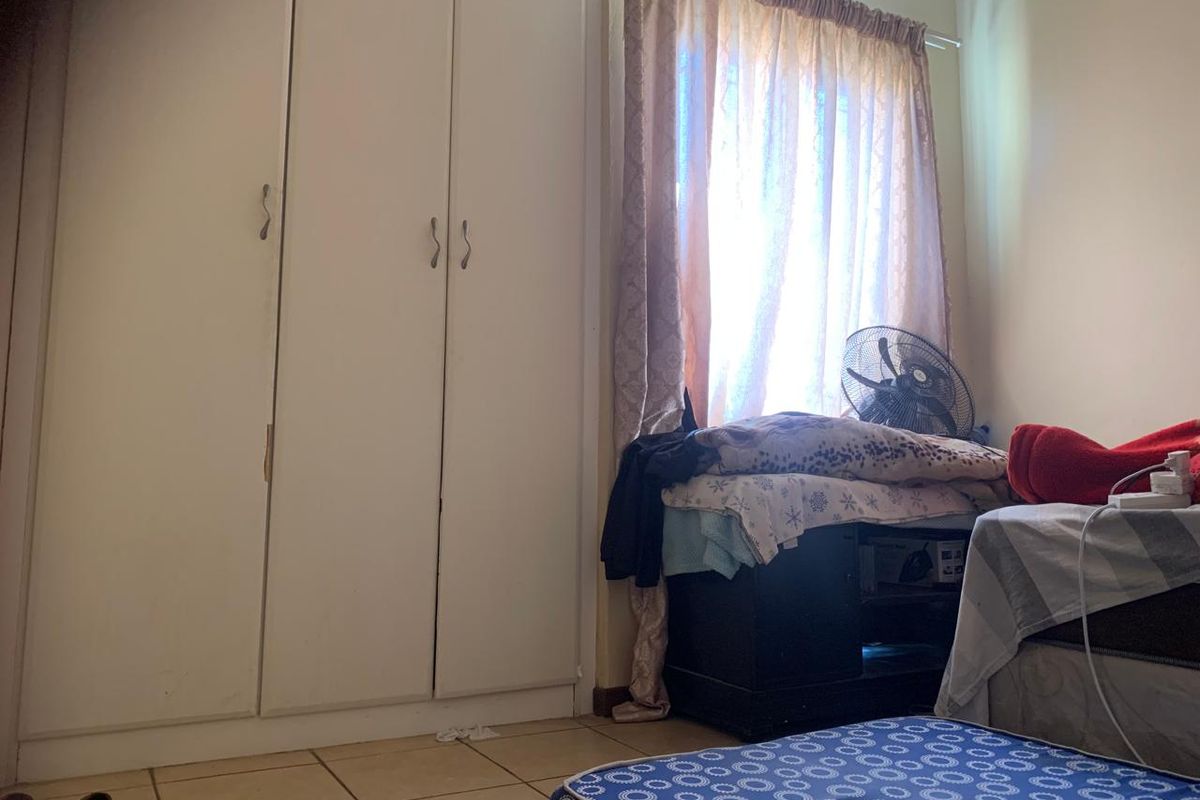 A bedroom featuring built-in cupboards and tiled flooring, offering a functional space with natural light from the window.