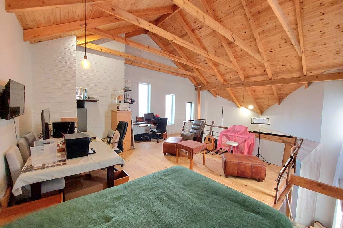 Spacious loft-style bedroom featuring exposed timber roof trusses, vaulted ceilings, and light wood flooring, creating an airy and open living environment.