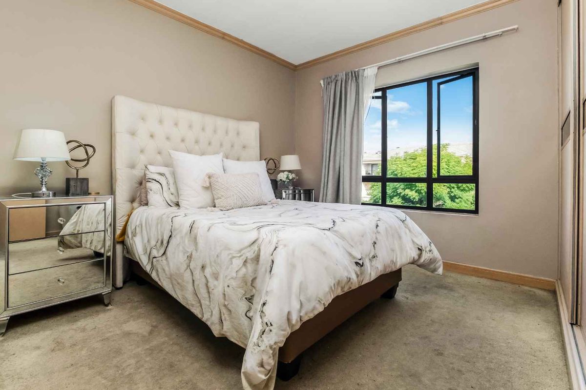 A well-lit bedroom featuring built-in wardrobes, neutral wall tones, and a large window providing natural light and exterior views.