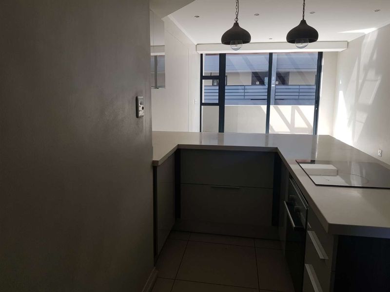 Modern kitchen featuring sleek cabinetry, stone countertops, built-in oven, and hob, with direct access to an outdoor area through sliding glass doors.