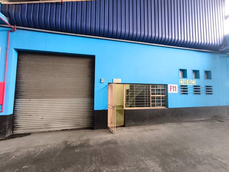 Industrial unit exterior featuring a large roller shutter door, security gate, and blue painted facade with fire exit signage.