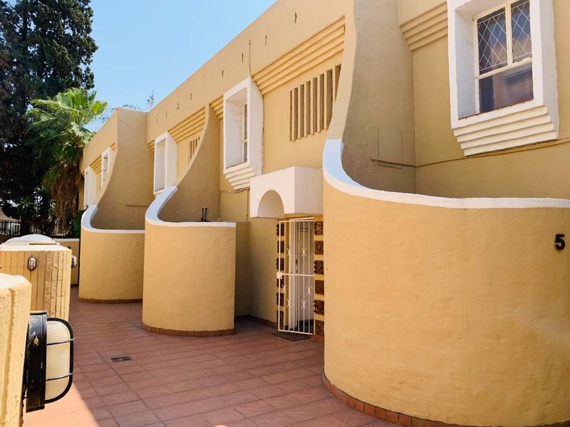 Front elevation of a townhouse complex featuring distinctive curved masonry walls, tiled patio area, and secure gated entrance.
