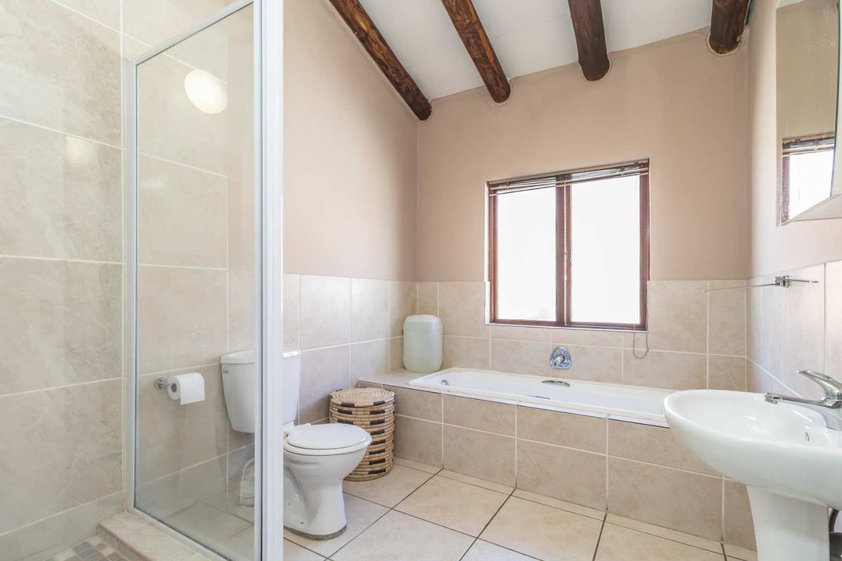 A functional bathroom featuring a glass-enclosed shower, a built-in bathtub with tiled surround, a pedestal sink, and exposed timber ceiling beams.