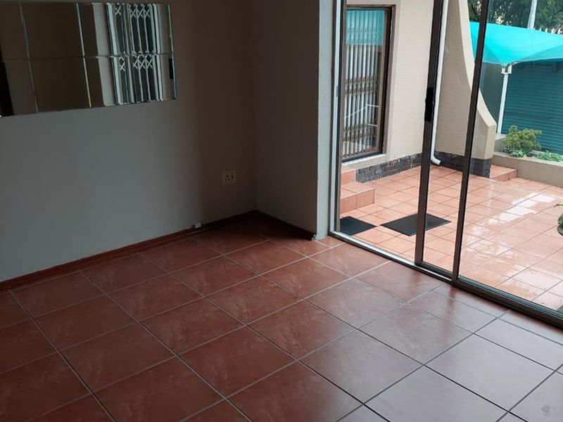 An empty living room featuring terracotta-style floor tiles and a large sliding glass door providing direct access to an outdoor patio area.