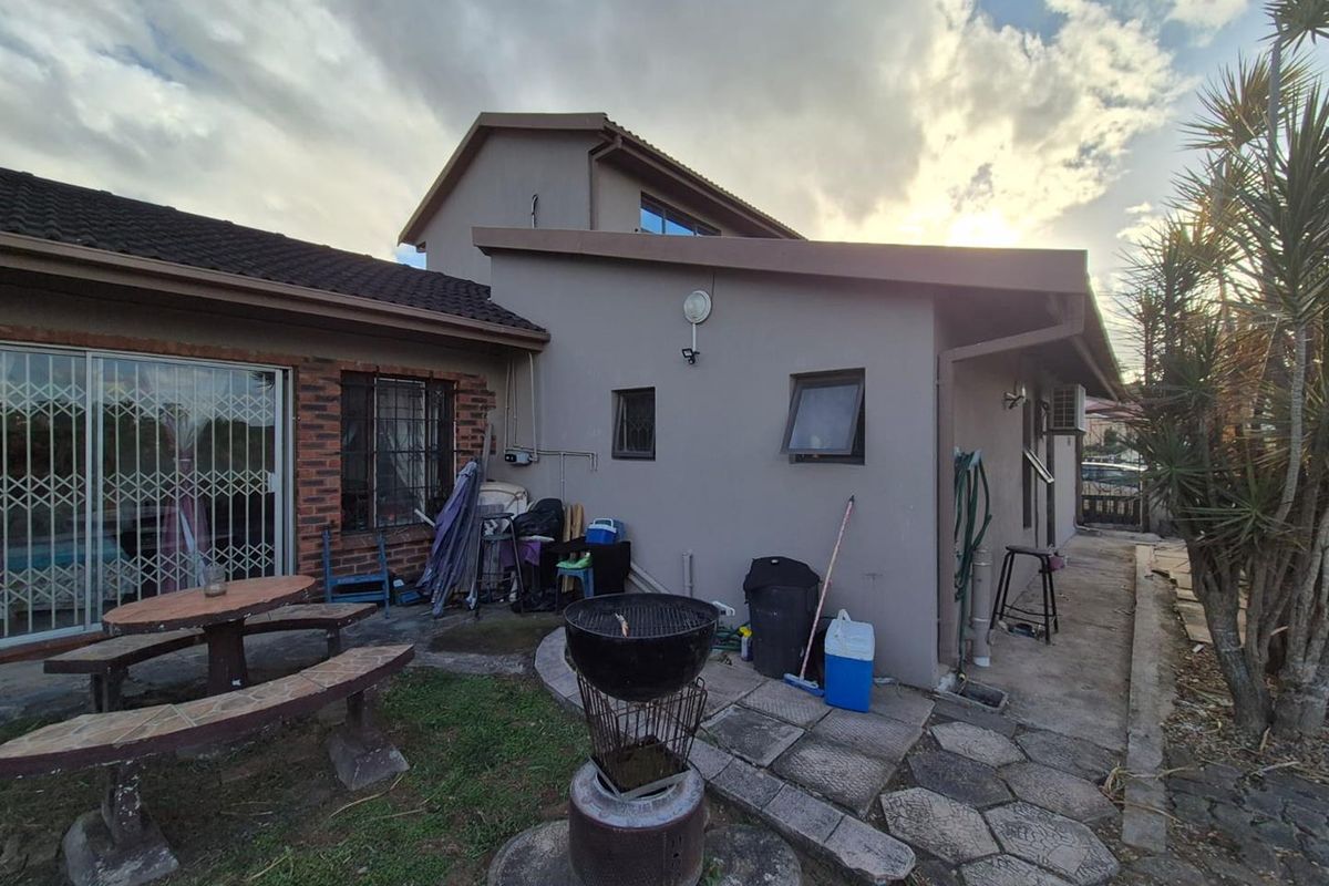 Rear exterior view of the house featuring a paved patio area, sliding glass doors with security gates, and a combination of brick and rendered walls.
