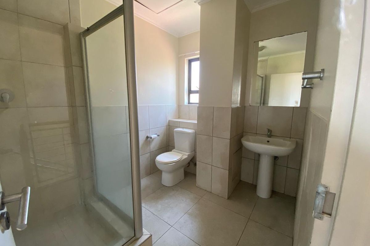 A functional bathroom featuring a shower enclosure, pedestal basin, and toilet with neutral wall and floor tiling.