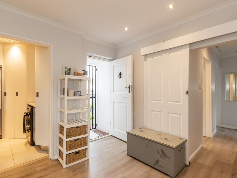 Bright and welcoming entrance hall featuring modern laminate flooring, recessed downlighting, and a secure entry door leading to the home interior.
