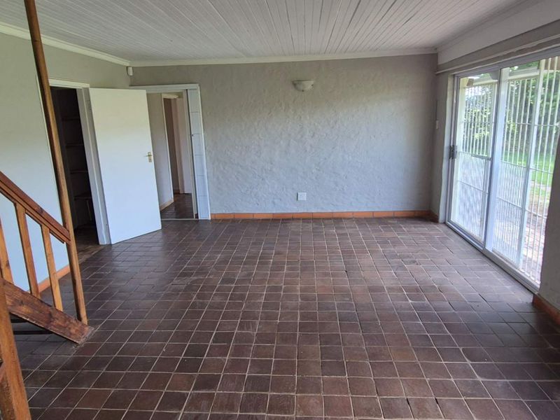 Spacious living area featuring terracotta tile flooring, a timber staircase, and large sliding glass doors providing access to the garden.