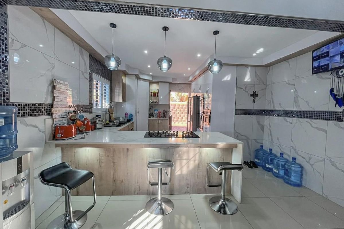 Modern kitchen featuring a central island with a built-in gas hob, marble-look wall tiling, and contemporary pendant lighting.