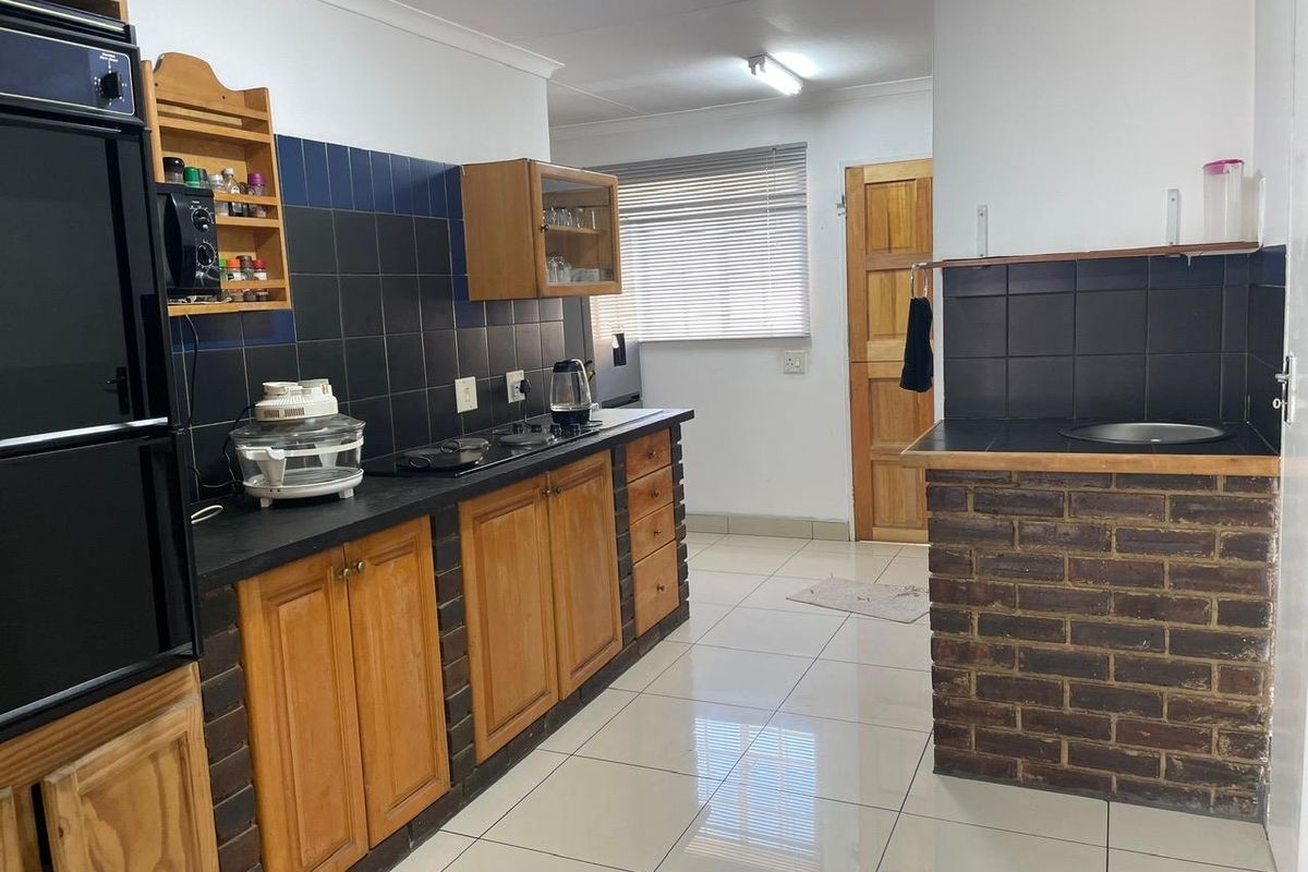 A functional kitchen featuring wooden cabinetry, dark tiled splashbacks, a built-in oven, and a brick-base breakfast counter with tiled flooring.