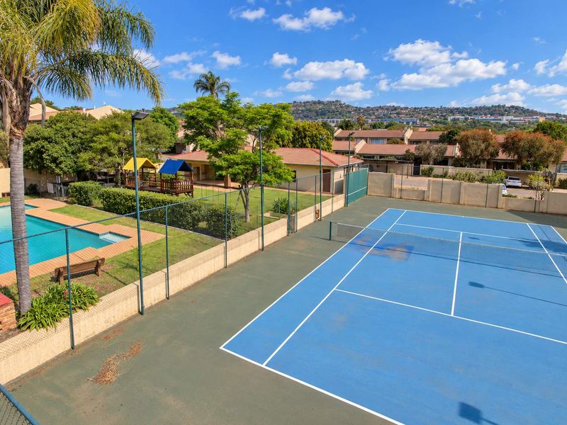 Aerial view of the complex communal facilities featuring a blue tennis court, swimming pool, and landscaped garden area.