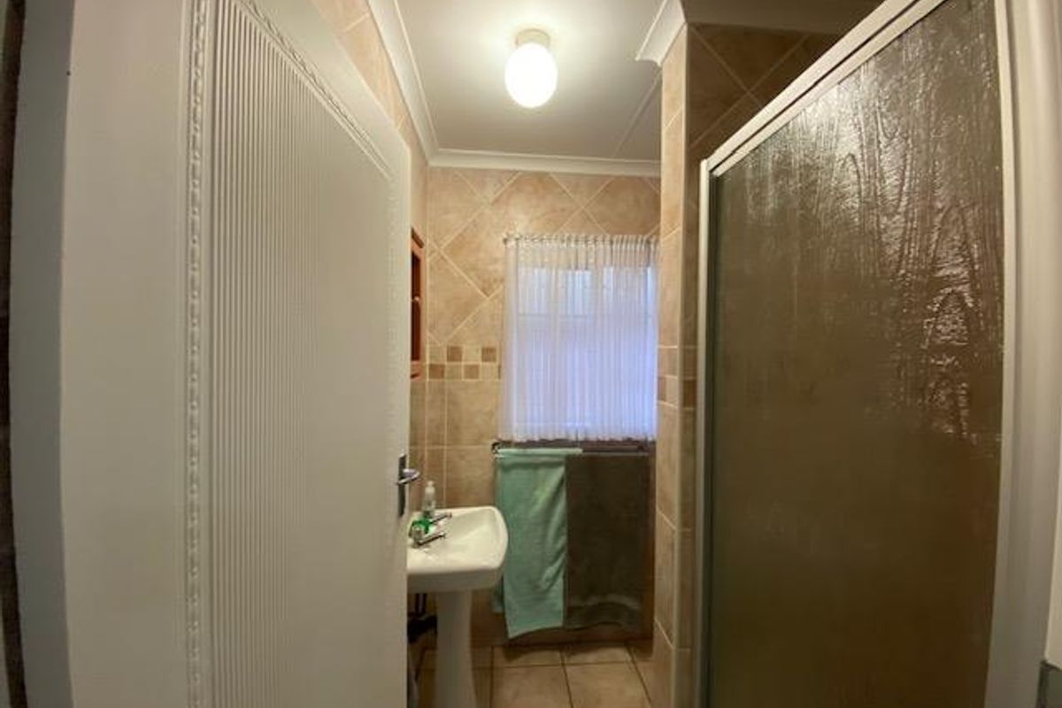 A functional bathroom featuring a pedestal sink, tiled walls and flooring, and a glass-enclosed shower unit.