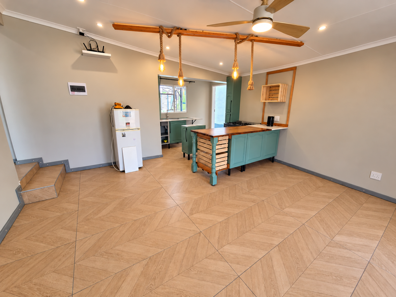 A bright, open-plan kitchen area featuring modern herringbone tile flooring, a custom kitchen island with pendant lighting, and neutral wall finishes.