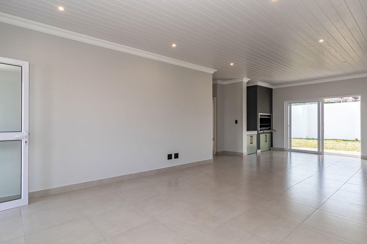 Spacious, modern open-plan living area featuring tiled floors, recessed lighting, a built-in braai, and sliding glass doors leading to the garden.
