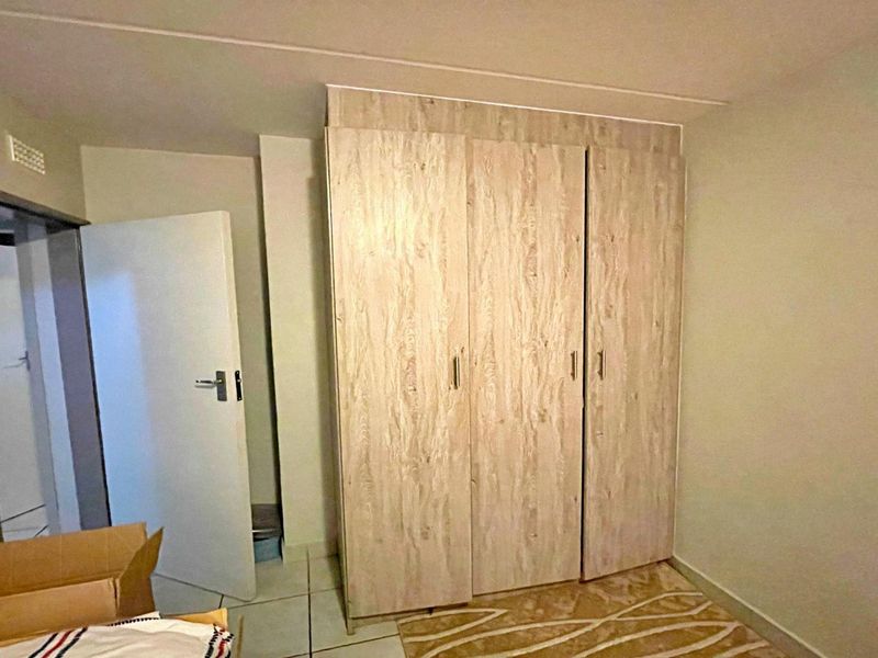 A bedroom featuring light wood-grain built-in wardrobes and neutral tiled flooring, offering a clean and functional space.