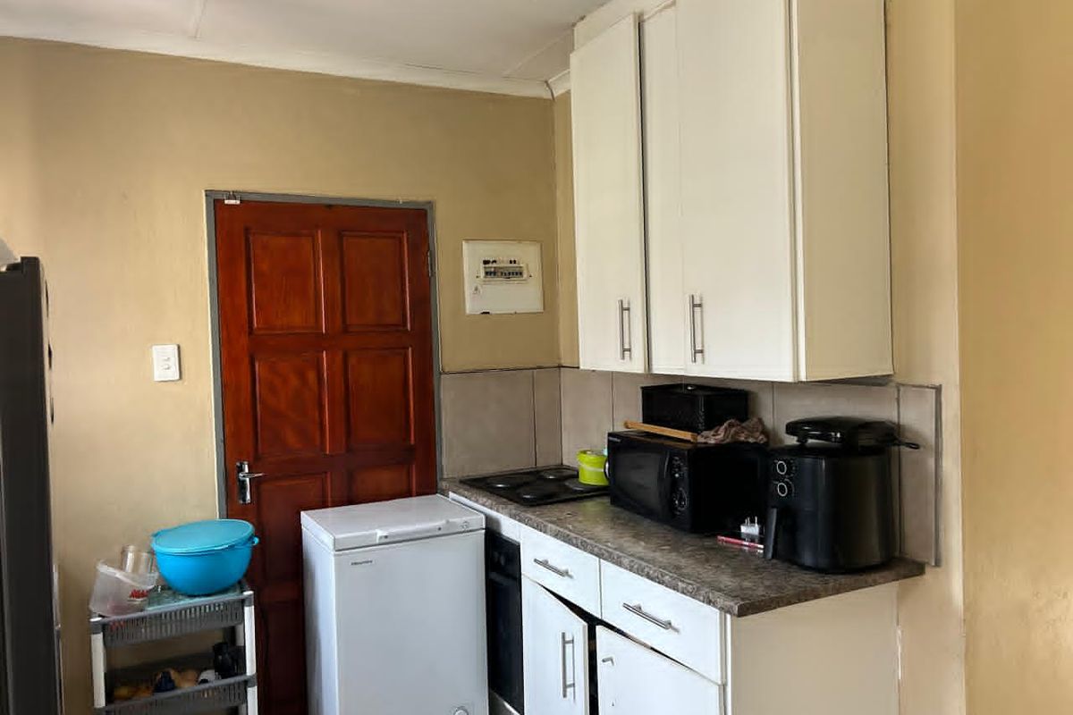 A functional kitchen area featuring white cabinetry, a built-in hob and oven, and a tiled splashback, providing essential cooking and storage space.