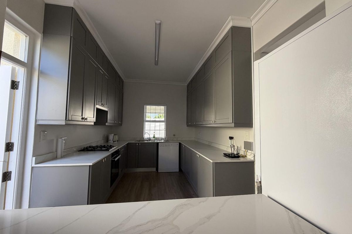 Modern galley-style kitchen featuring grey cabinetry, stone countertops, built-in gas hob, oven, and integrated dishwasher.