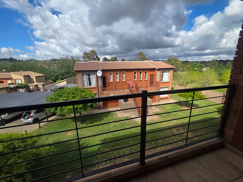 A spacious balcony featuring a metal balustrade and tiled flooring, offering an elevated view of the surrounding residential complex and garden area.