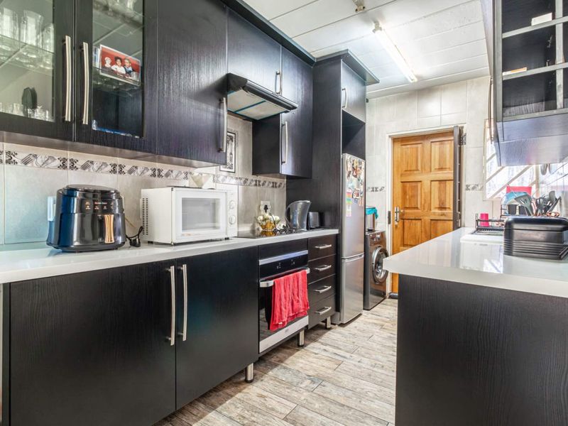 A functional kitchen featuring dark wood cabinetry, white stone countertops, built-in oven, extractor fan, and tiled flooring with direct access to an exterior door.