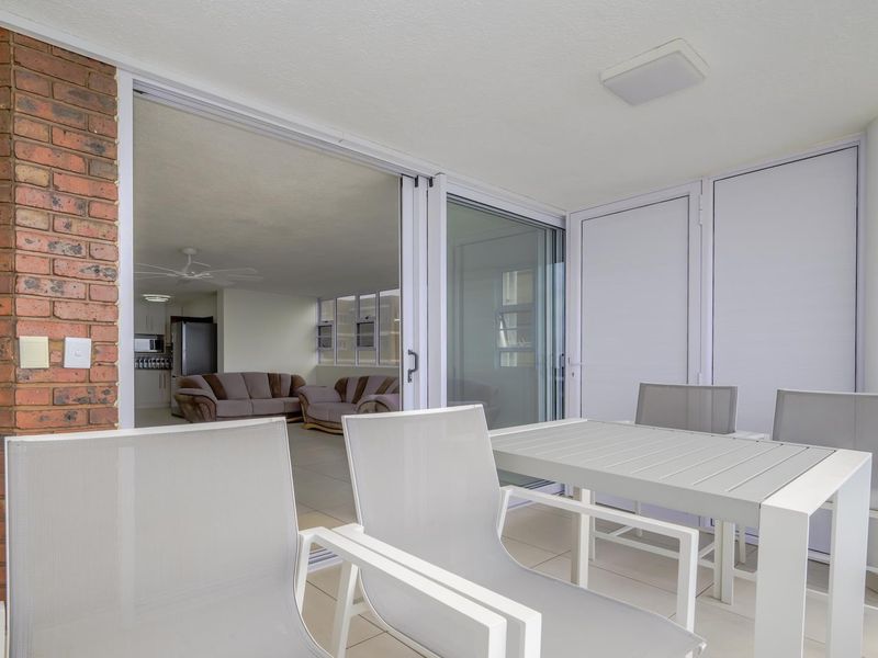 A covered balcony featuring tiled flooring, an exposed brick accent pillar, and large sliding glass doors providing access to the interior living area.