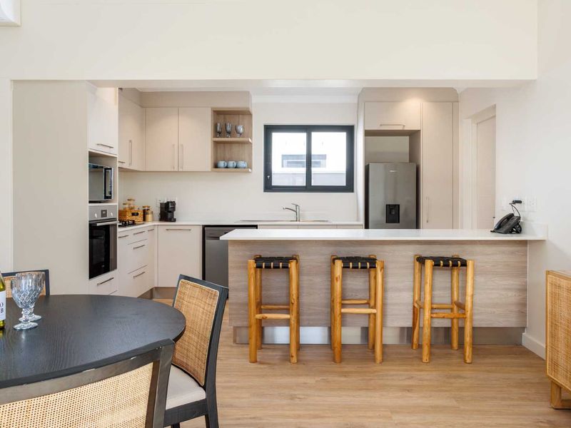 Modern open-plan kitchen featuring sleek cabinetry, stone countertops, integrated appliances, and a functional breakfast bar, seamlessly connecting to the dining area.