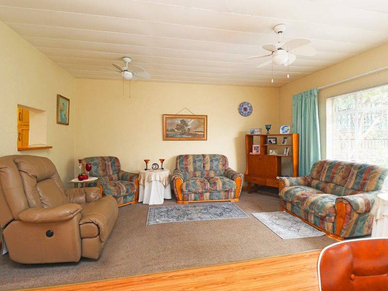 A spacious living room featuring a combination of carpet and timber-look flooring, dual ceiling fans, and a convenient pass-through window to the kitchen area.
