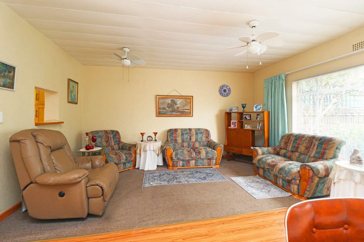 A spacious living room featuring a combination of carpet and timber-look flooring, dual ceiling fans, and a convenient pass-through window to the kitchen area.