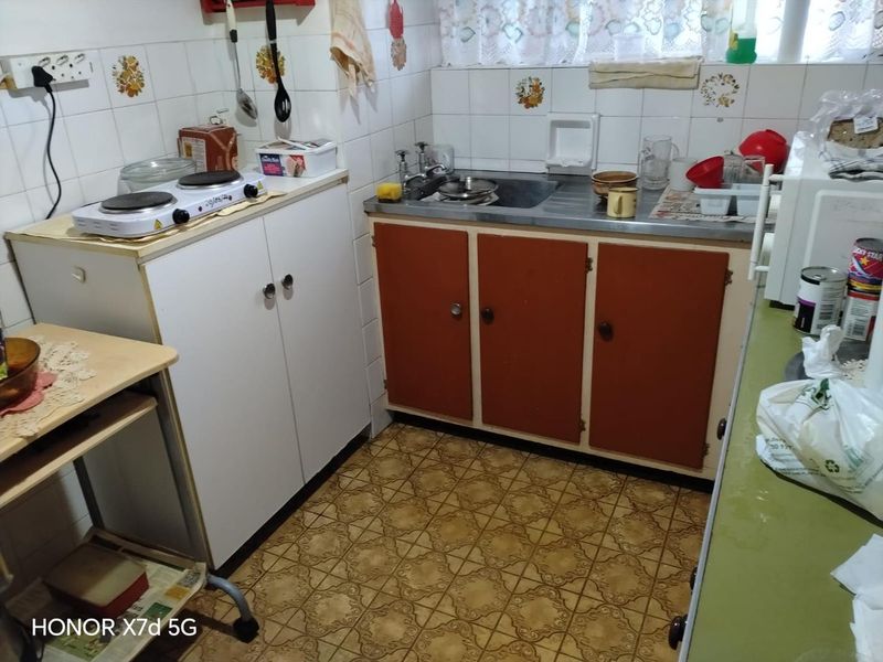 A compact, dated kitchen featuring original cabinetry, a stainless steel sink, and tiled backsplash, offering significant potential for modernization and renovation.