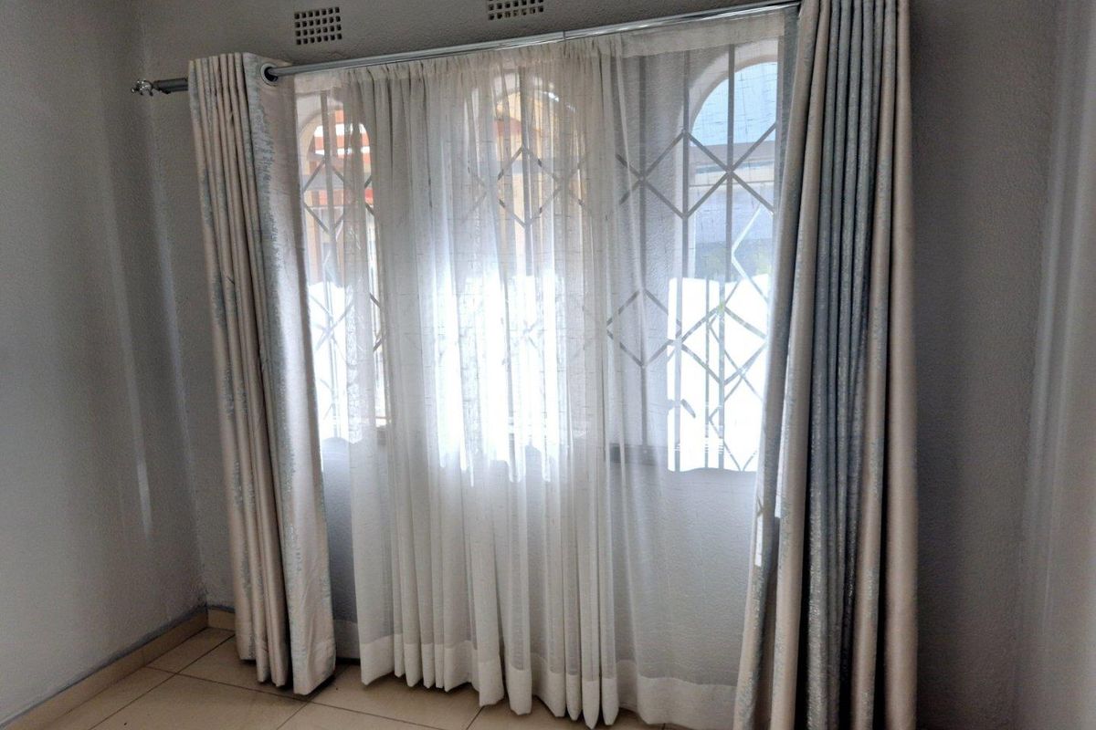 A bright, empty bedroom featuring tiled flooring, a curtain rod, and security gates on the windows.