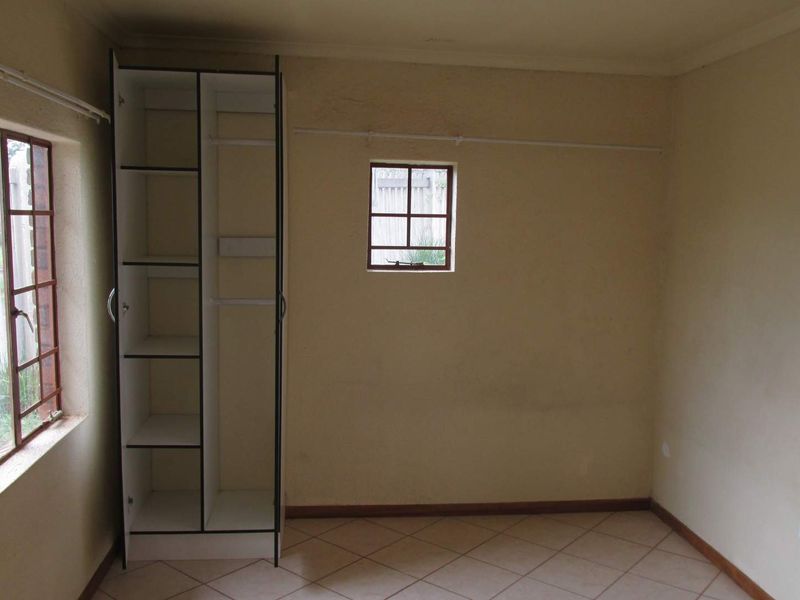 A compact bedroom featuring tiled flooring, a built-in cupboard, and security bars on the windows. The room is vacant and ready for updates.
