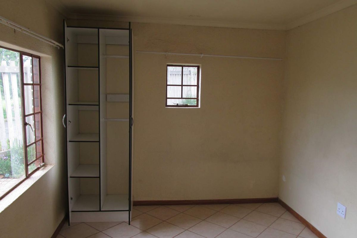 A compact bedroom featuring tiled flooring, a built-in cupboard, and security bars on the windows. The room is vacant and ready for updates.