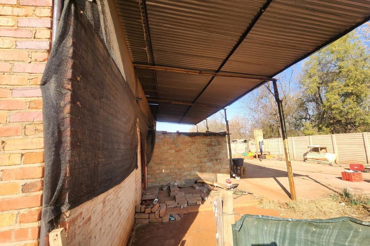 Rear exterior area featuring a corrugated metal roof structure over an unfinished brick wall and open yard space with precast boundary walling.