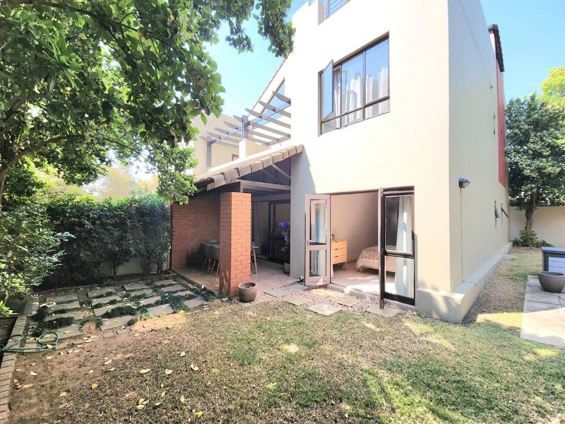 Rear view of the apartment featuring a covered patio with brick pillars, a timber pergola, and direct access to the garden through sliding doors.