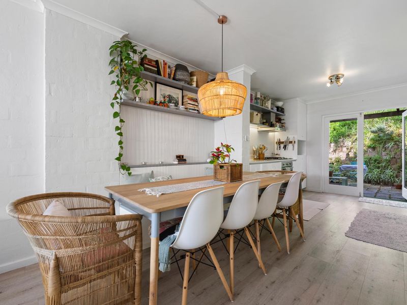 Bright open-plan dining and kitchen area featuring built-in shelving, modern pendant lighting, and direct access to a rear garden through glass sliding doors.