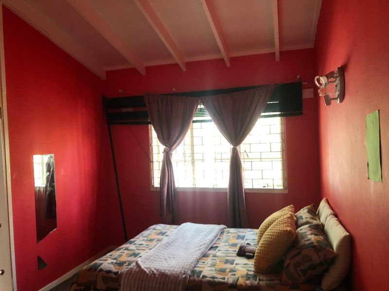 A bedroom featuring an exposed beam ceiling and a window fitted with security bars, currently finished with bold red wall paint.