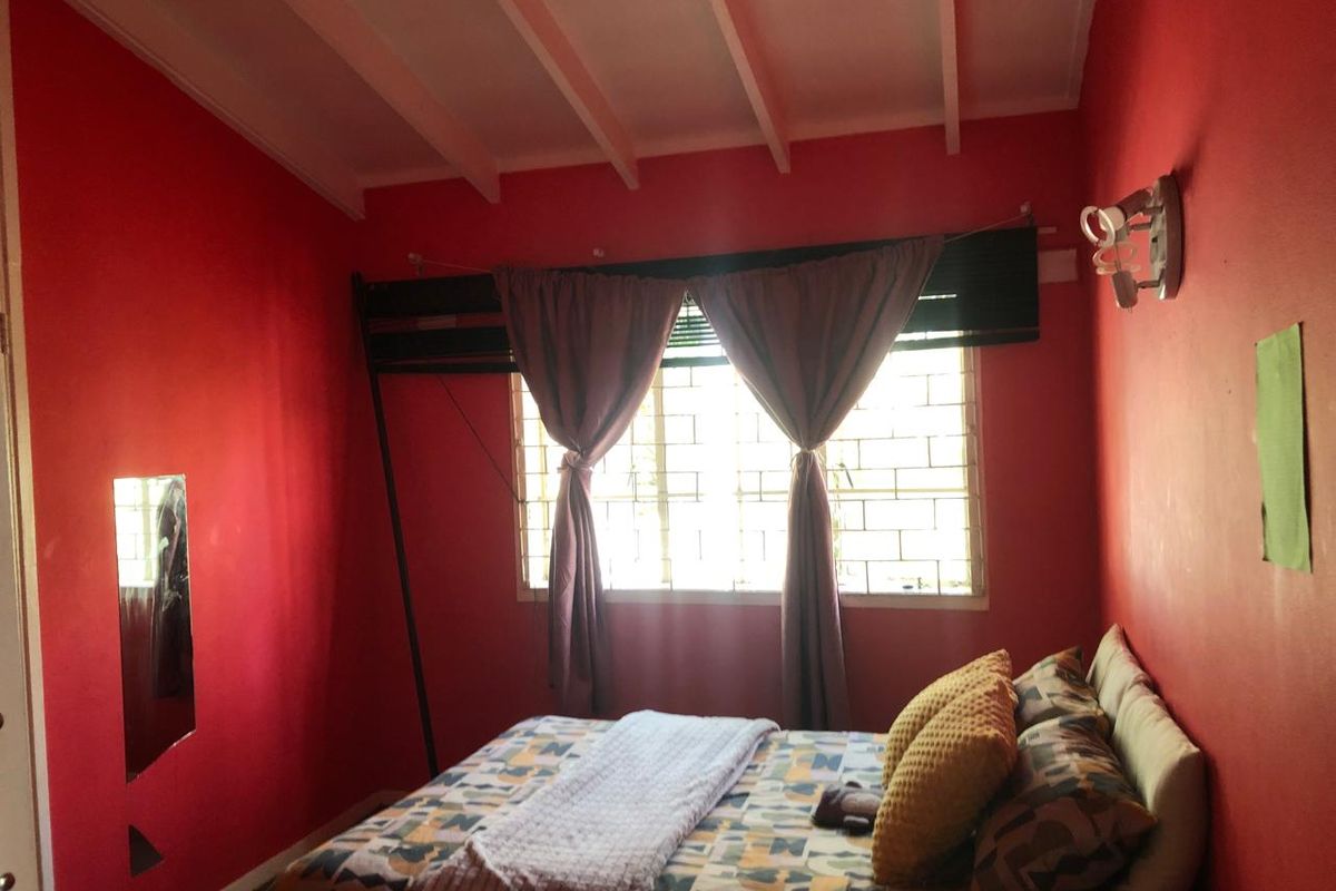 A bedroom featuring an exposed beam ceiling and a window fitted with security bars, currently finished with bold red wall paint.