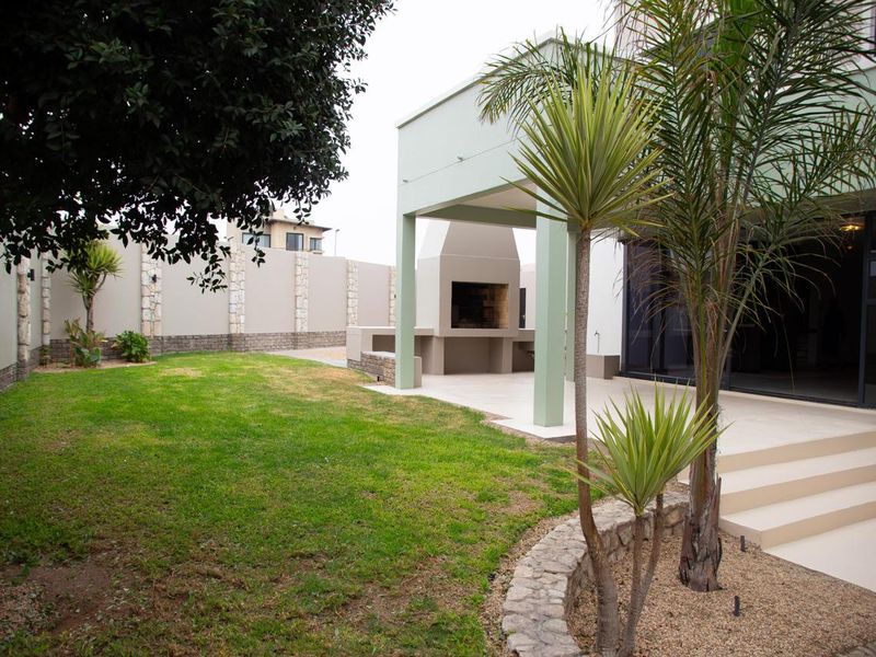 A covered patio area featuring a built-in braai, tiled flooring, and direct access to the rear garden through large sliding glass doors.
