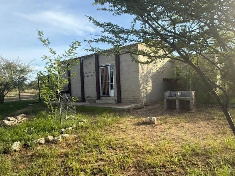 Rear view of the farm dwelling featuring a concrete patio, built-in braai area, and security gate access.