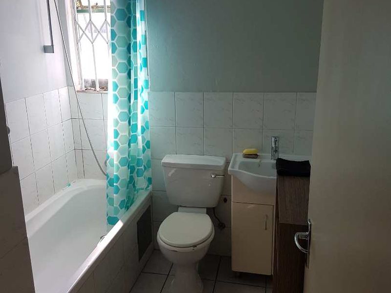 A functional bathroom featuring a bathtub with shower mixer, a standard toilet, and a vanity basin with tiled finishes.